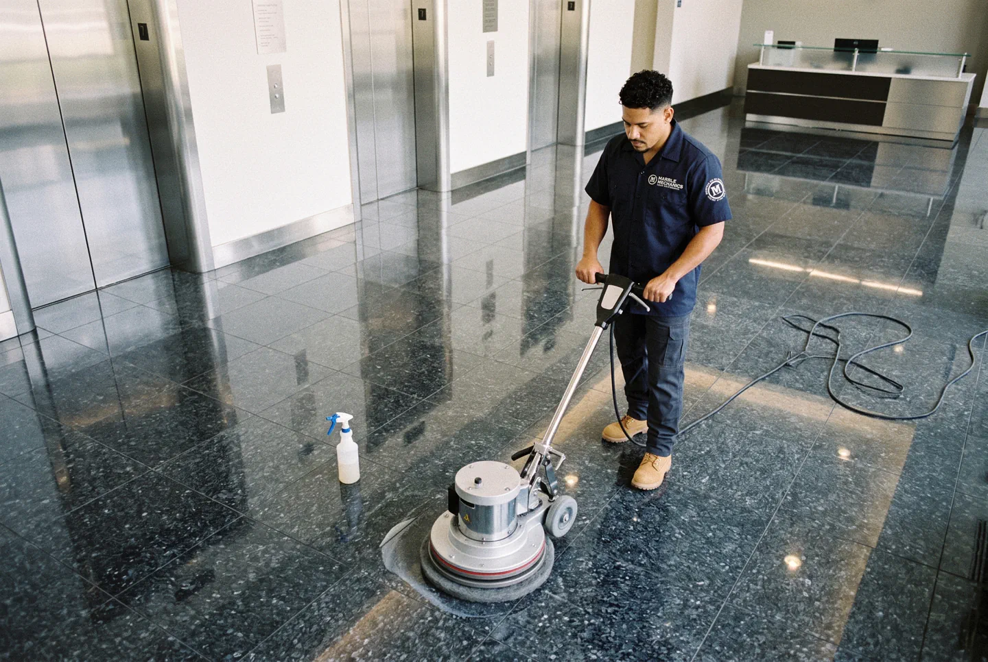 Commercial granite restoration in Tampa: a Marble Mechanics technician running a floor machine across a granite elevator lobby