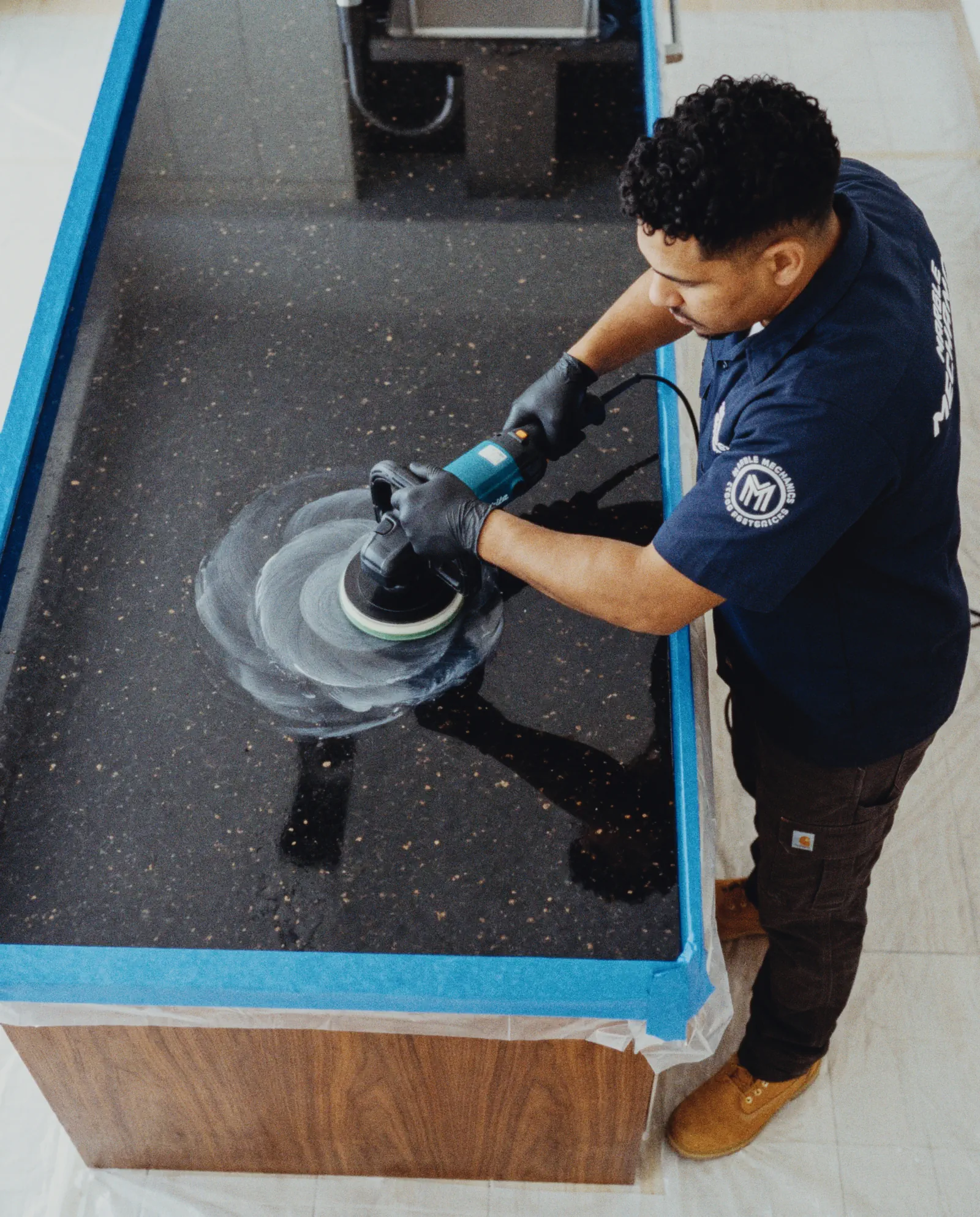Granite restoration in Tampa: a Marble Mechanics technician polishing a black granite island countertop with a rotary polisher, the edges masked off