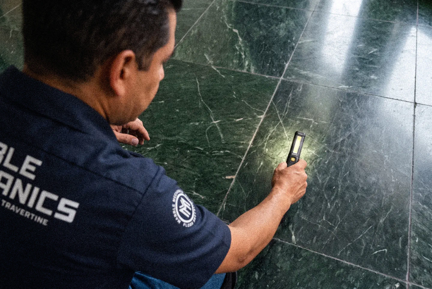 Marble Mechanics technician inspecting a green marble floor with a raking work light before restoration begins