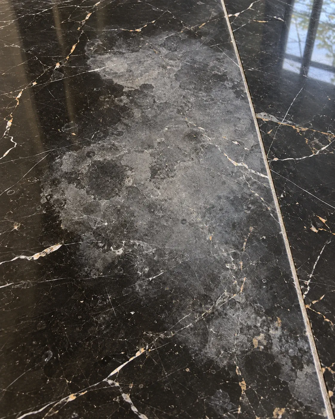 Etched, blotchy black marble tile where acid has burned through the polish, before restoration in Tampa Bay
