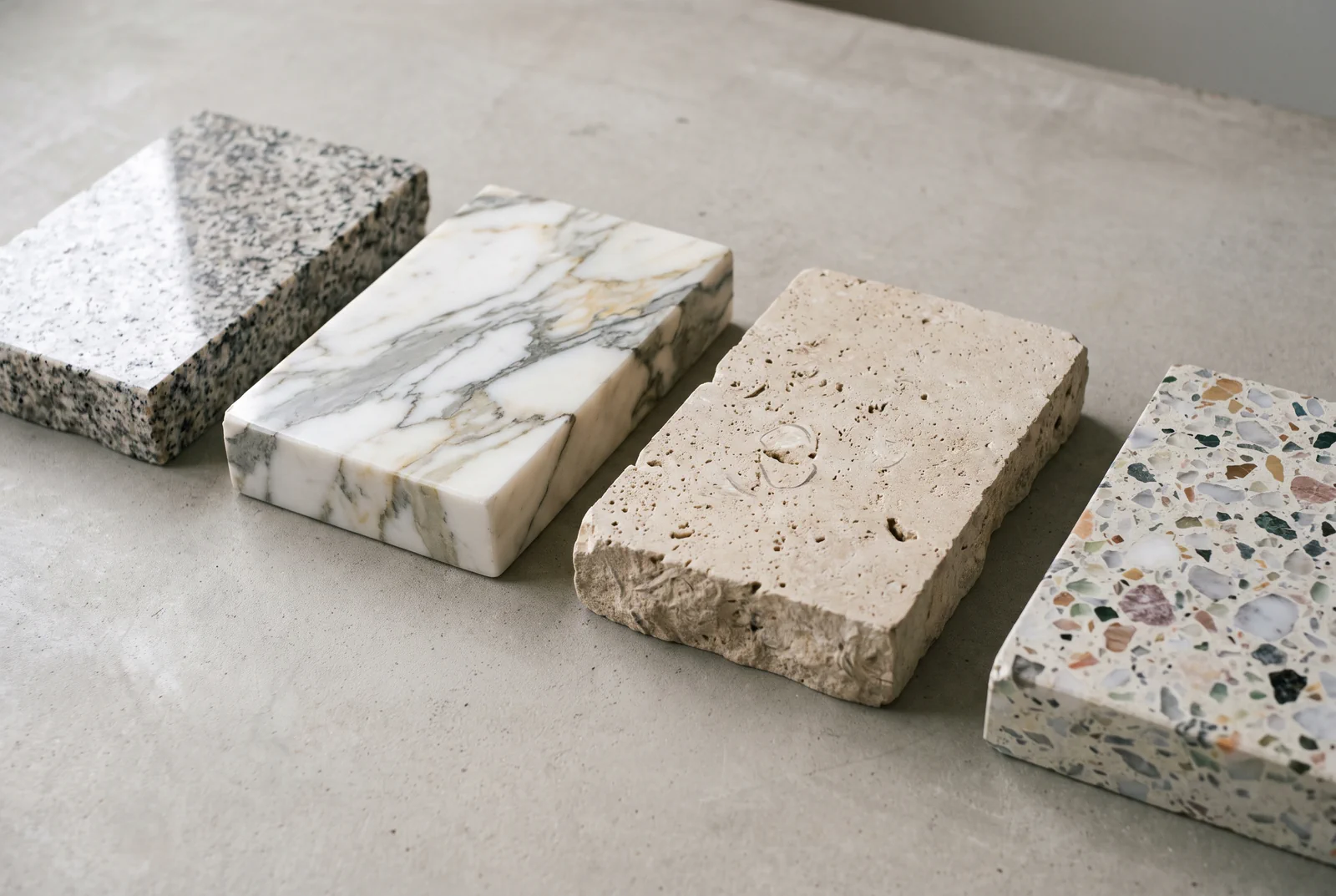 Granite, marble, travertine and terrazzo samples side by side, with water beading on the travertine
