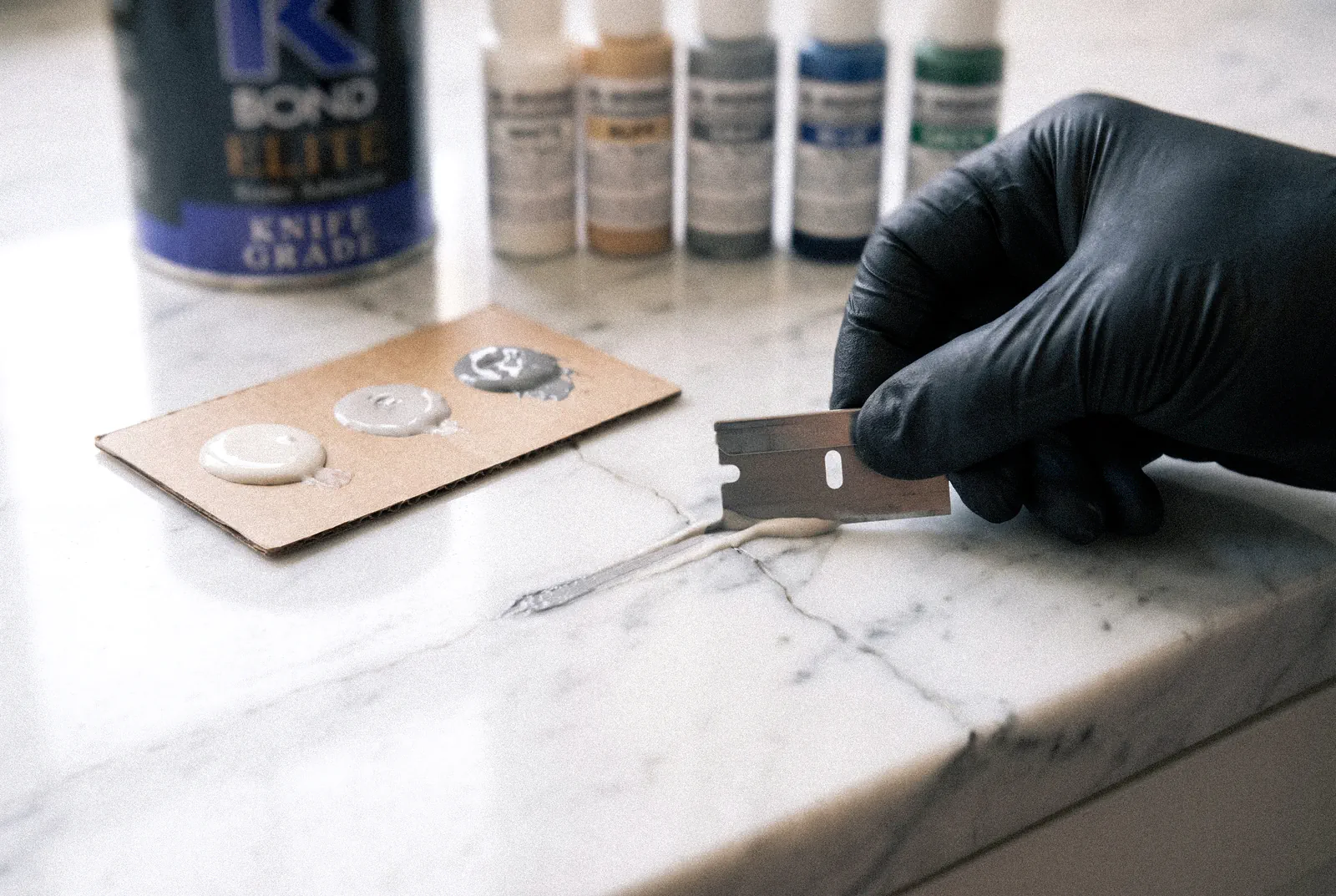 Stone countertop polishing in Tampa: color-matched epoxy drawn flush into a crack on a white Carrara marble countertop, with the pigment bottles beside it